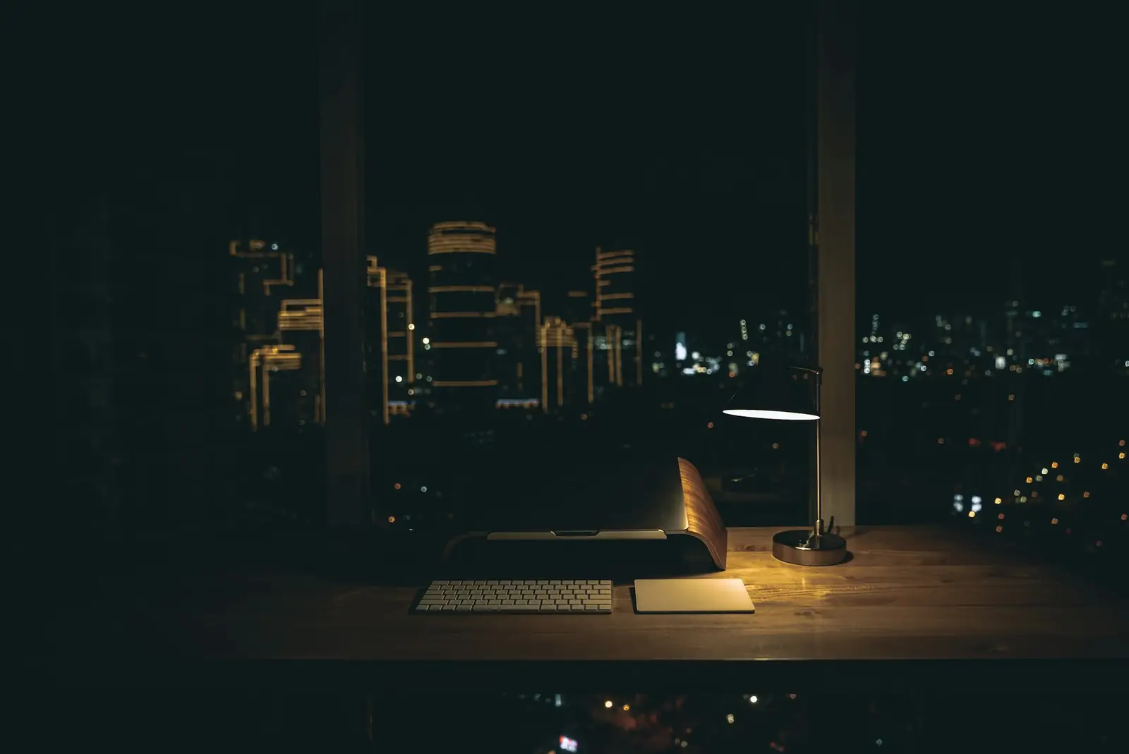 Escritorio con una lámpara encendida en una oficina vacía de noche, con la ciudad iluminada detrás